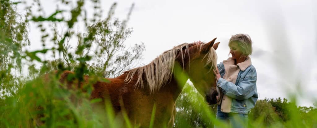 Blije vrouw houdt paard vast in groene weide, contact en vriendschap tussen mens en dier in de natuur.